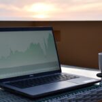 A laptop displaying a financial graph on a table with a coffee cup beside it during sunset