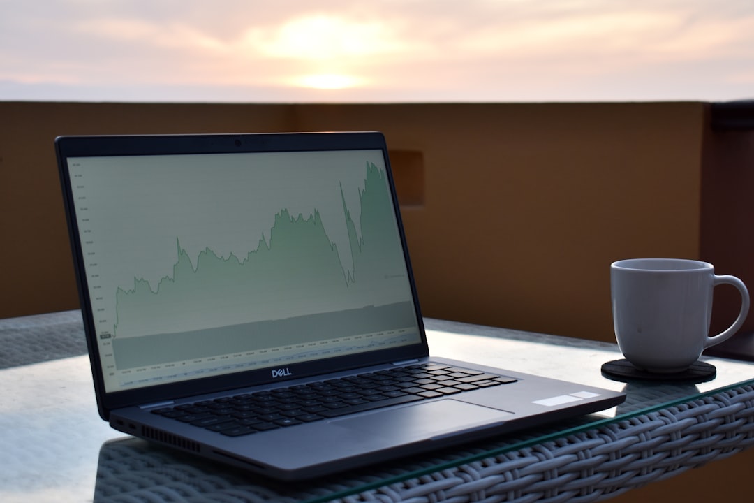 A laptop displaying a financial graph on a table with a coffee cup beside it during sunset
